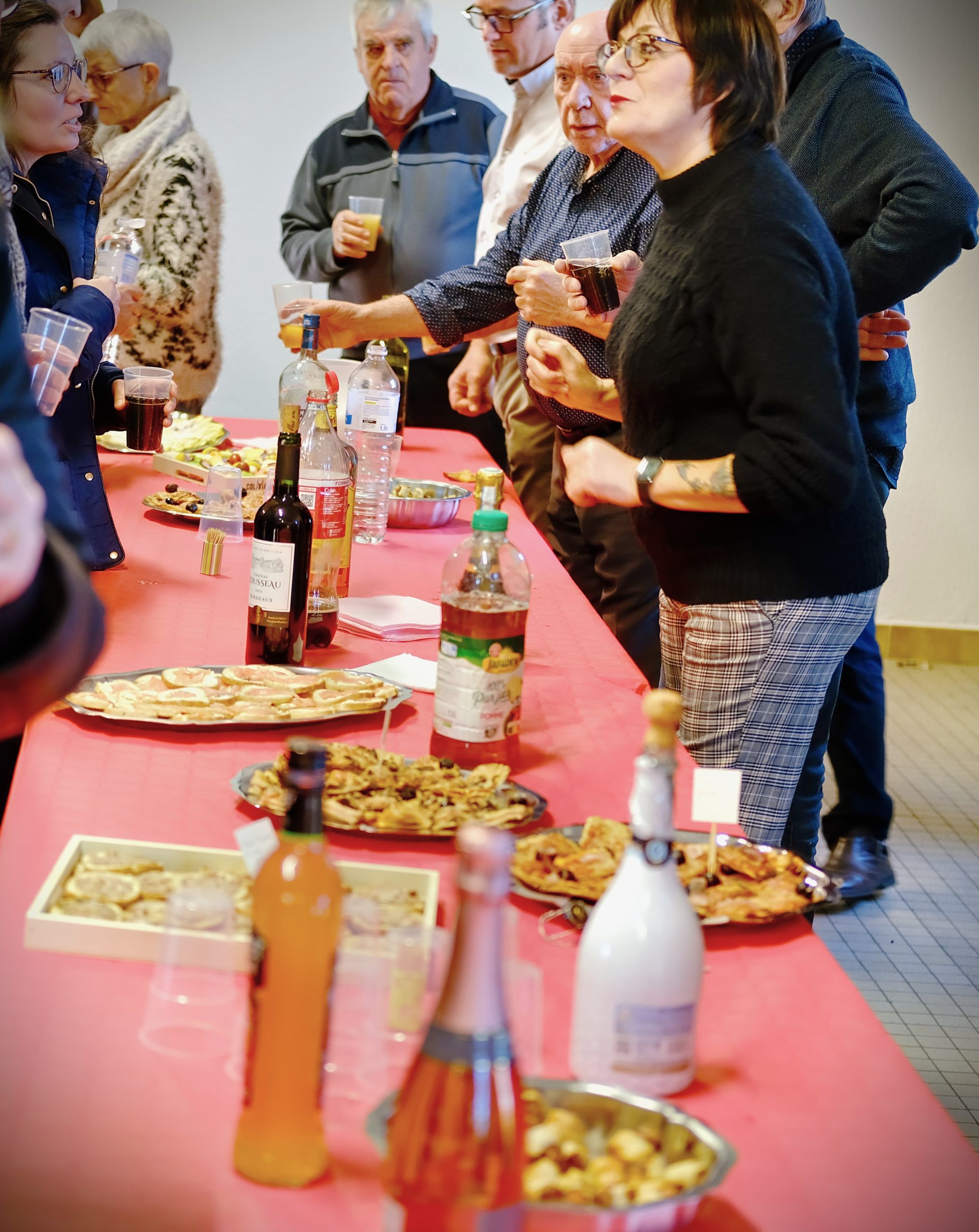 buffert servi lors de la cérémonie avec des bouteilles de mousseux, de jus de fruits et des petits fours. Un groupe de personne parle ensemble en arrière plan.