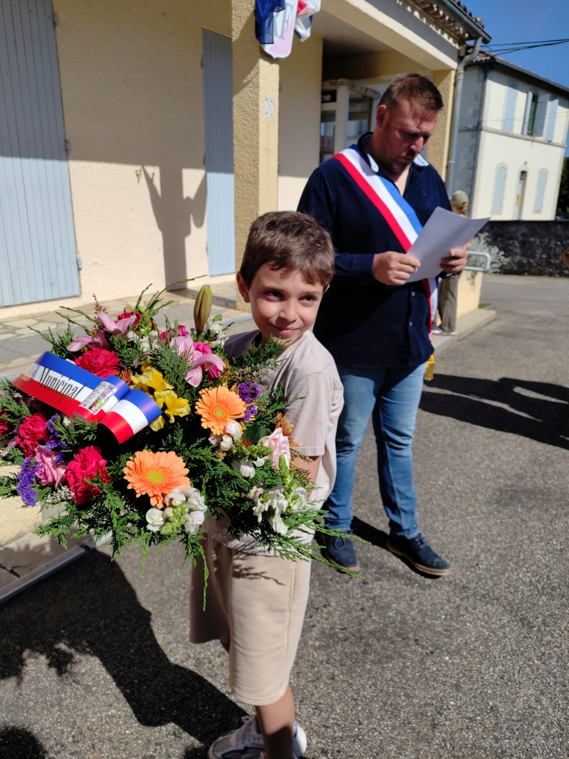 Le jeune Kaïs tenant la gerbe de fleurs destinée au monument aux morts de Frespech lors du 8 mai 2026