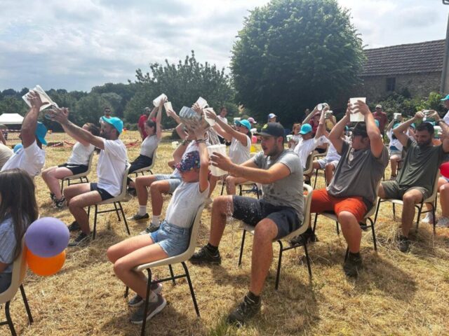 Des participants passent un seau au dessus de leur tête dans une course assise