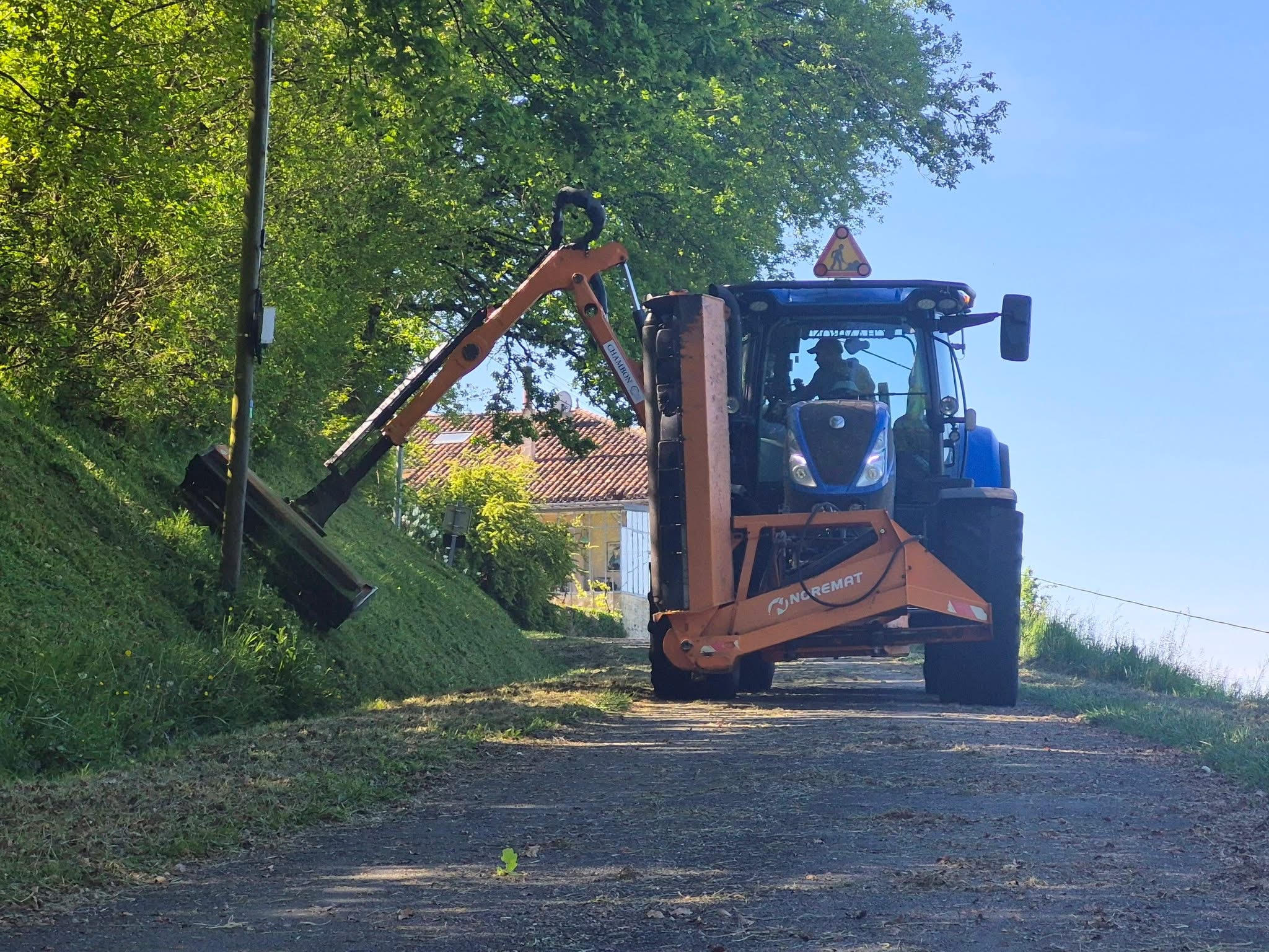 engin de fauchage en train de couper les bords d'une route de campagne